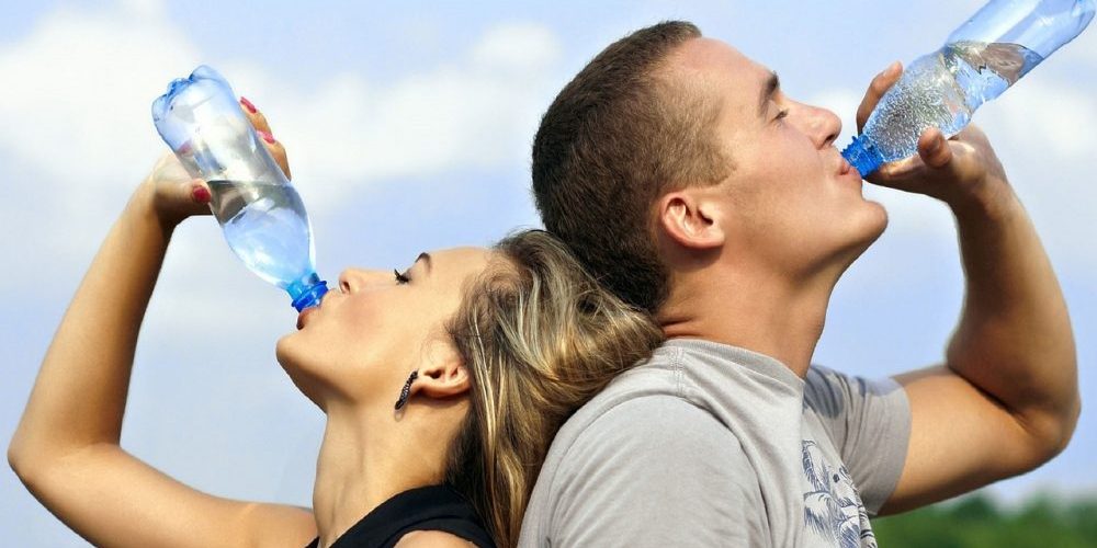 Homem e mulher a beber água de garrafas de plástico, promovendo a alimentação saudável