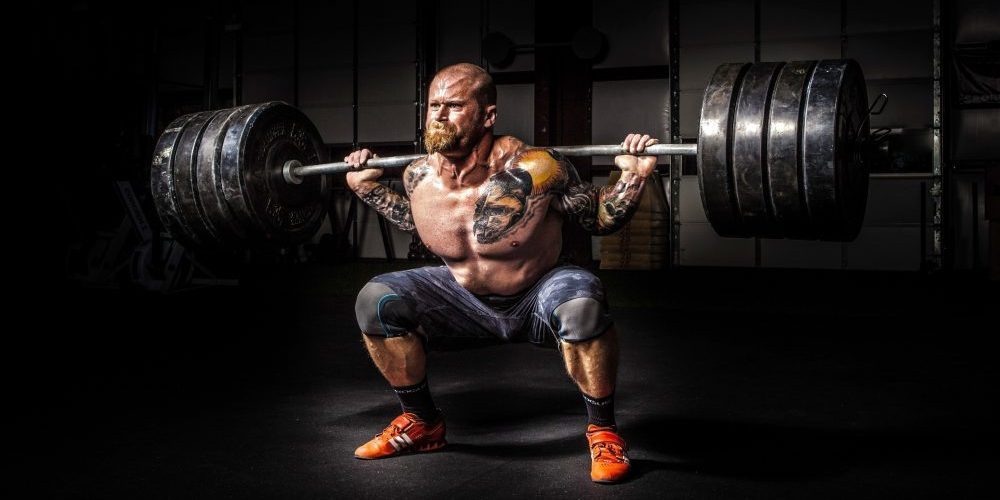 Homem executa um squat ou agachamento com barra